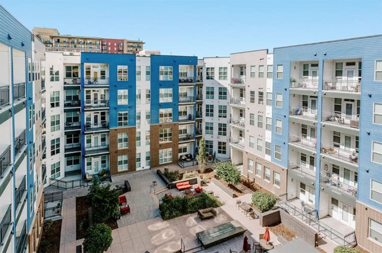 Modern multi-story apartment complex with courtyard and outdoor communal space.